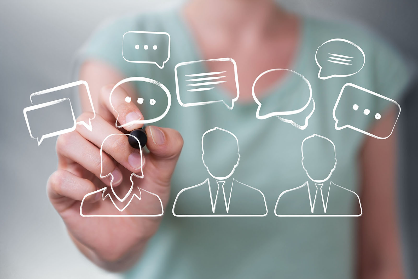 Die rechte Hand einer Frau im grünen T-Shirt hält einen schwarzen Stift in den Vordergrund, wo drei Personen mit Sprechblasen gezeichnet sind.