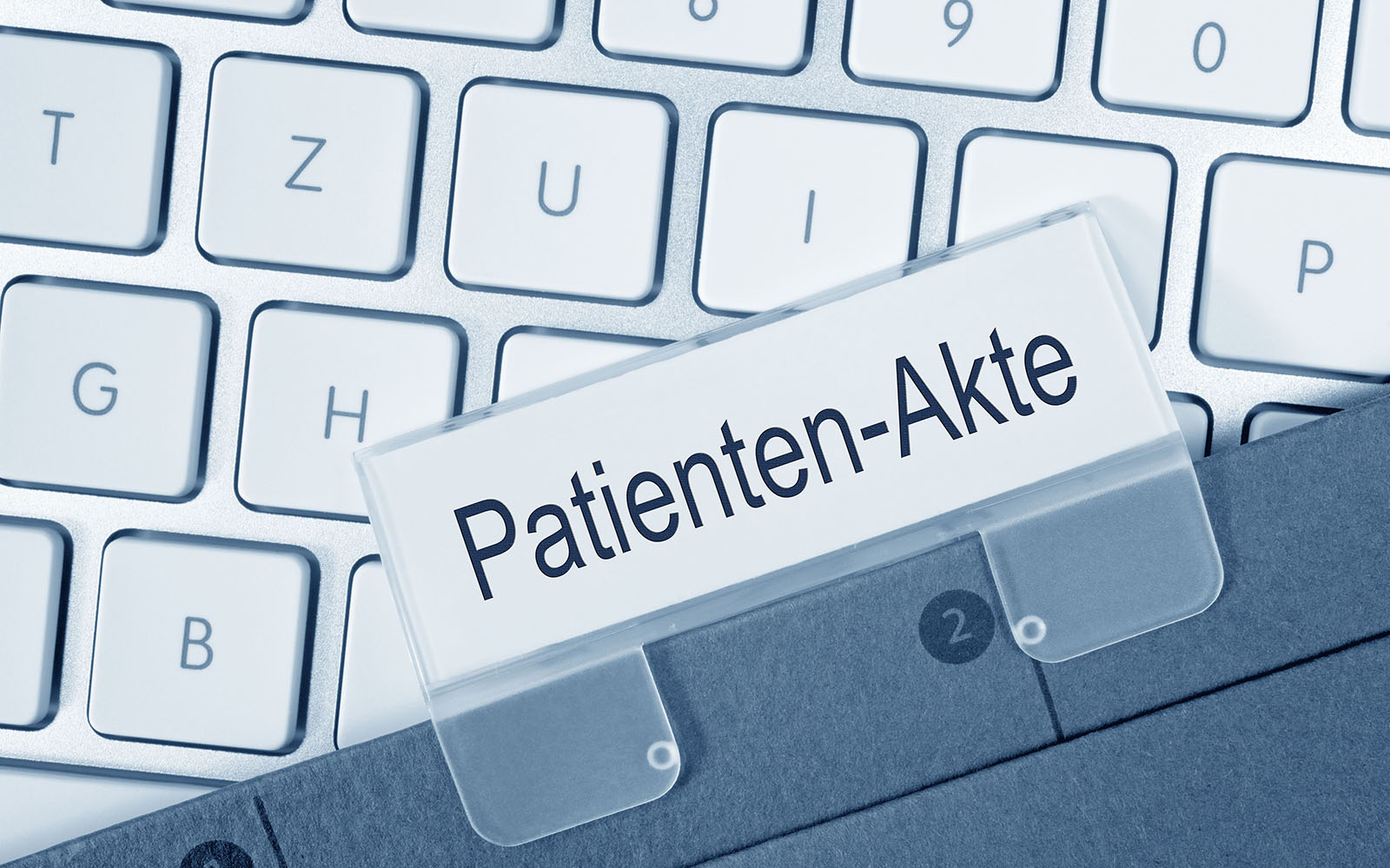 Der Ausschnitt einer weißen Tastatur, auf der eine graue Patientenakte liegt.